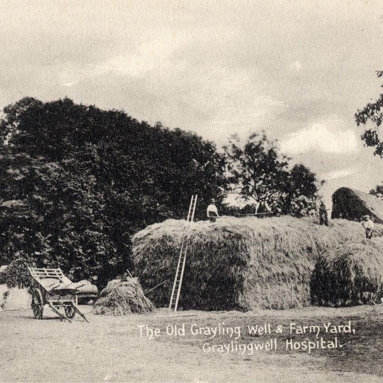 An old image of hay stacks and two workers at Graylingwell Farm Yard